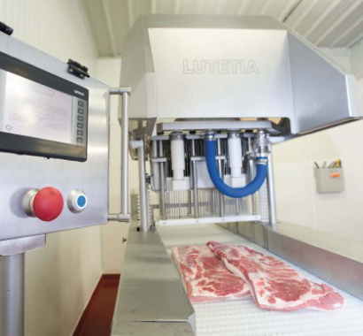 Moved via a conveyor, the whole muscle cut of raw bacon is about to receive an injection and massage of a brine solution on custom equipment built by Lutetia.