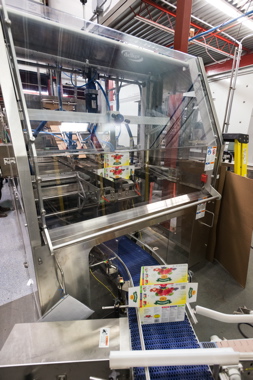 A Delkor Trayfecta S Series carton former discharging Club-style cartons onto the StrongPoint-supplied conveyor system diverting it to a robotic case-packer.