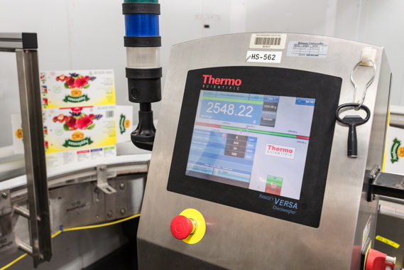 A Thermo Scientific Ramsey VERSA checkweigher quickly checks and verifies the weight of full cases of Applesnax applesauce before closing the flaps to ensure each contains the pre-determined number of product packs.